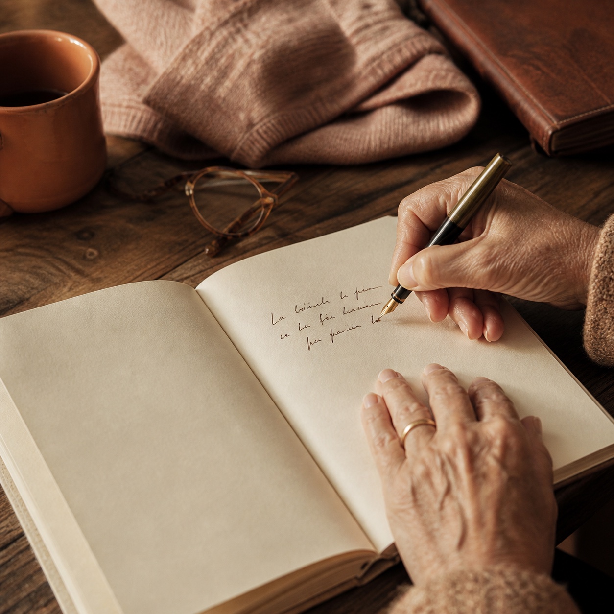 An end-of-career desk, closed binder and soft lamp, on a corner of wooden table; an open notebook and a fountain pen wait beside it.